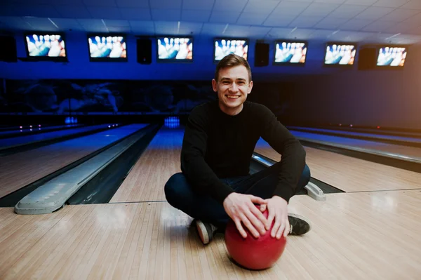 Cheerful young man holding a bowling ball and smiling at camera