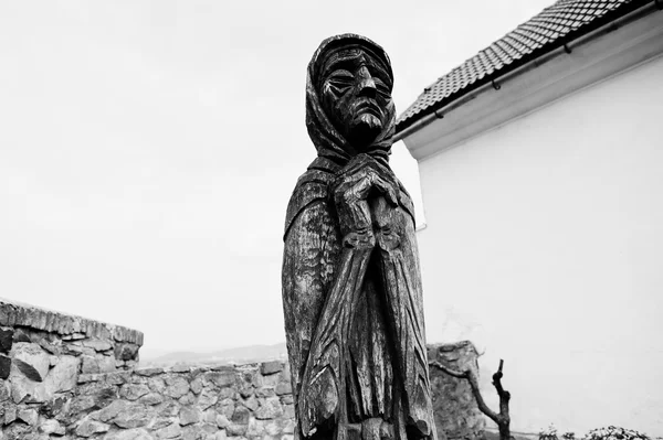 Wooden statue of old sad praying woman. Black and white