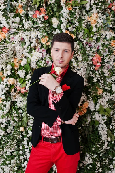 Fashion young man with rose at hand, in black suit and red pants