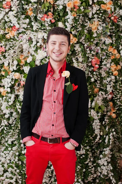 Fashion young laughing man with rose , in black suit and red pan