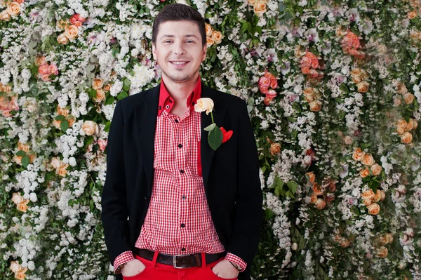 Fashion young laughing man with rose , in black suit and red pan