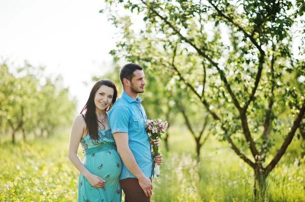 Happy pregnant couple at turquoise dress on the garden