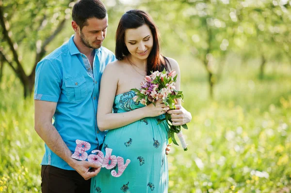 Happy pregnant couple at turquoise dress on the garden