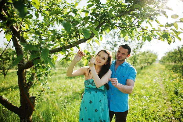 Happy pregnant couple at turquoise dress on the garden