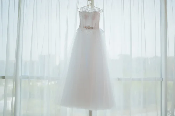 Beautiful white wedding gown hanging by window