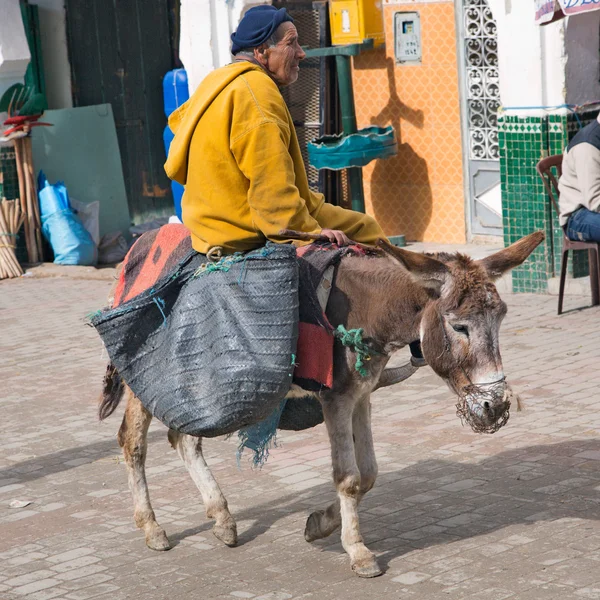 Man in yellow jacket riding on donkey