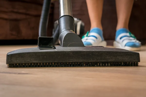 Woman with vacuum cleaner cleaning wooden laminate floor