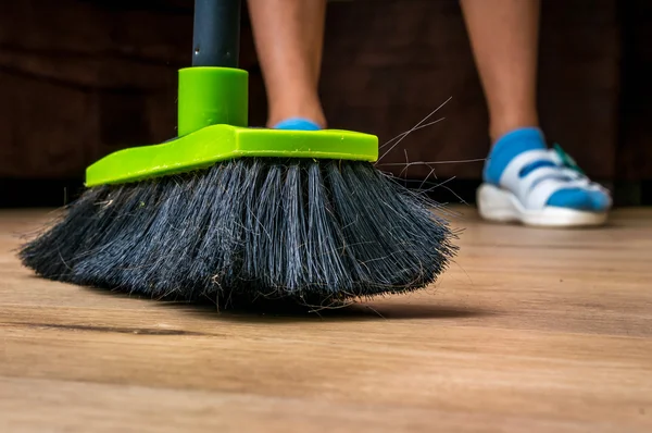 Woman with broom sweeping wooden laminate floor