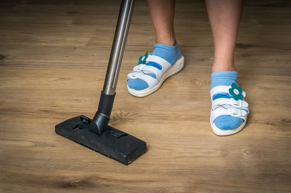 Woman with vacuum cleaner cleaning wooden laminate floor