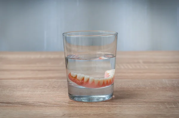 False teeth swim in transparent water glass