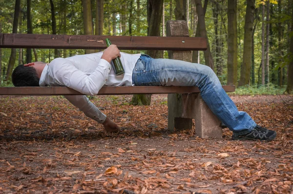 Drunk man asleep on a park bench with beer bottles