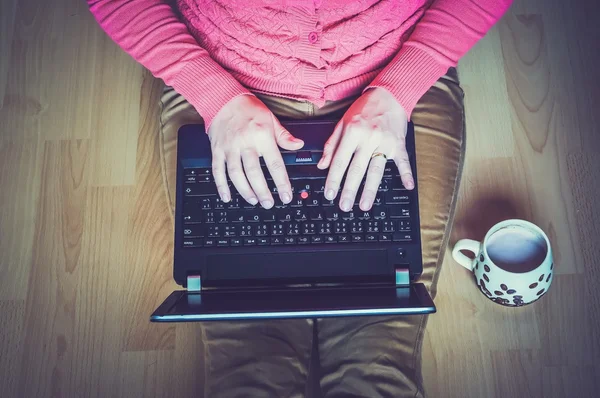 Young student using a laptop and sitting on the wooden floor in a classroom