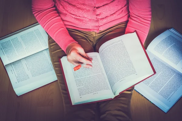 Young woman on the wooden floor in the library reading a book, studying