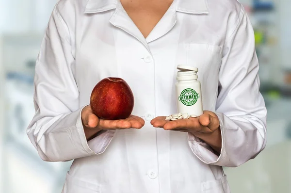 Young doctor holding apple and bottle of pills with vitamins and compare them