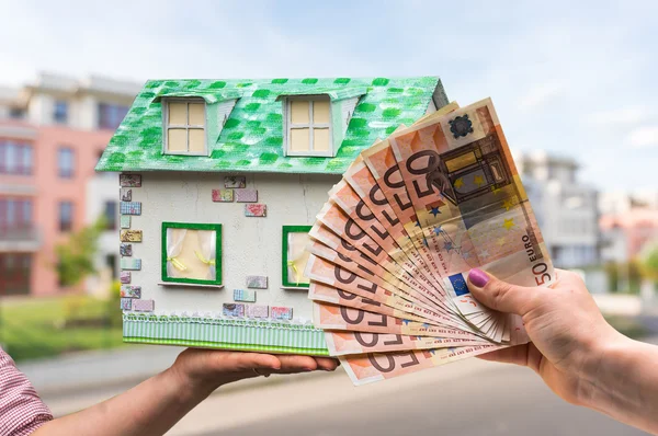 Real estate agent holding model house from paper and new property owner buying it by euro money