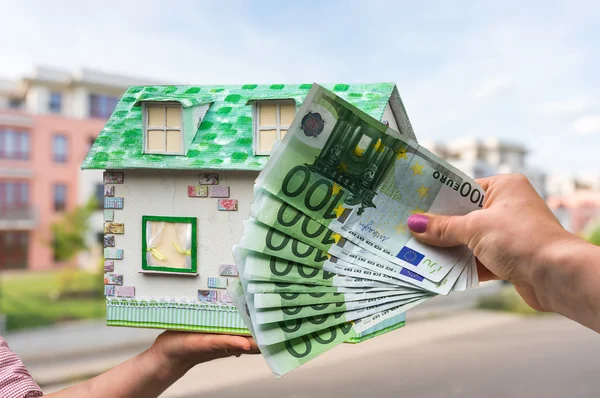 Real estate agent holding model house from paper and new property owner buying it by euro money