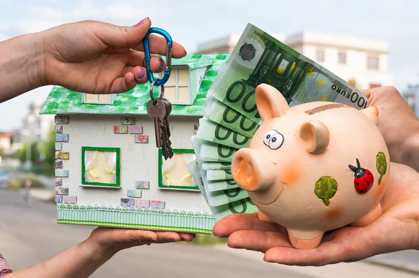 Real estate agent giving house key and model house to a new property owner, who is paying by euro money from piggy bank