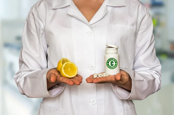 Young doctor holding two halves of lemon and bottle of pills with vitamins and compare them