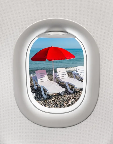 Looking out the window of a plane to the sunbeds and umbrella