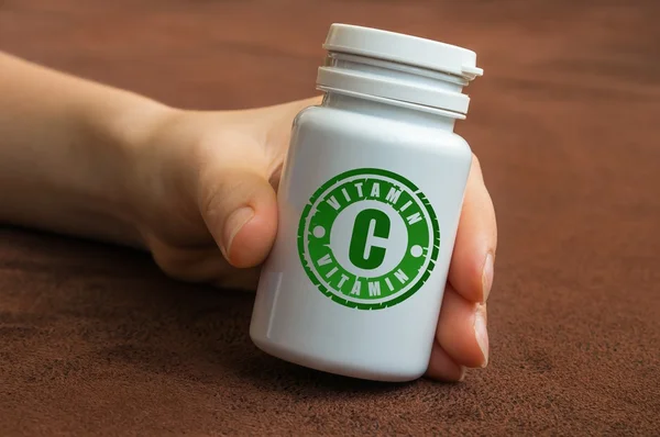 Human hand holding a bottle of pills with vitamin C