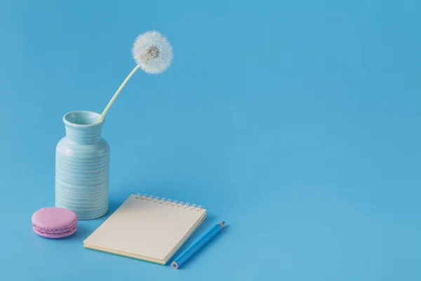 Notebook, pencil, dandelion on blue desk background