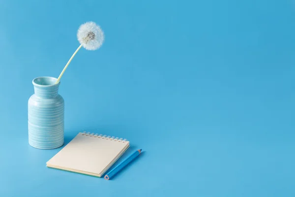 Notebook, pencil, dandelion on blue desk background