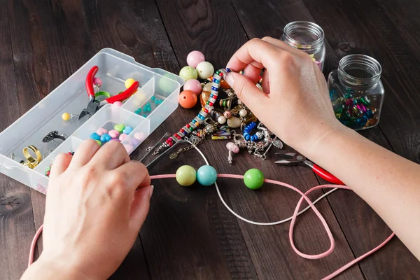 Pair of hands and pliers assembling a bead necklace.