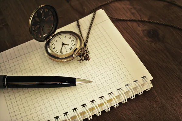 Notebook with blank pages, black pen and vintage pocket watch on wooden background