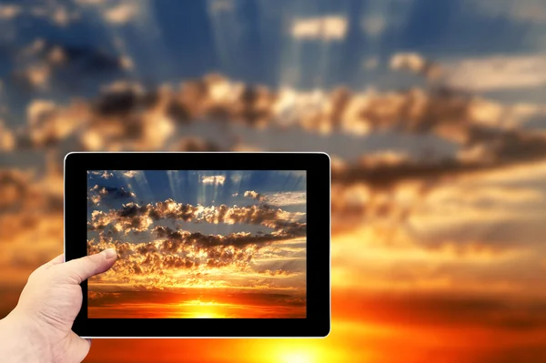 Tablet photography concept. Taking pictures on a tablet. Beautiful blue cloudy sky with golden red sunset and rays of light