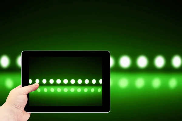 Tablet photography concept. Taking pictures on a tablet. Play of green light on defocusing blur led lamps background