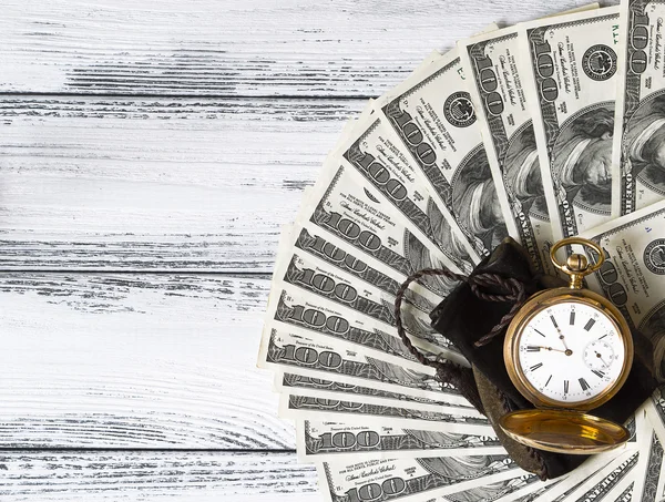 Stack of money dollars laid out like a fan with antique gold watch on white retro stylized wood background