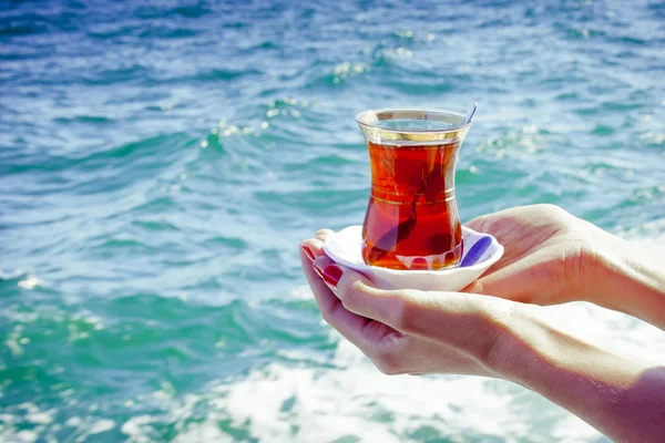 A glass of Turkish tea in the hands on the background of the Bosphorus in Istanbul, Turkey. Стакан турецкого чая в руках на фоне Босфора в Стамбуле, Турция.