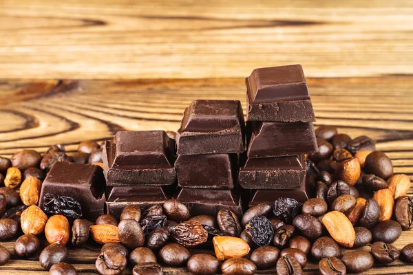 Dark chocolate cubes, coffee beans, peanuts and raisins on wooden table, close-up