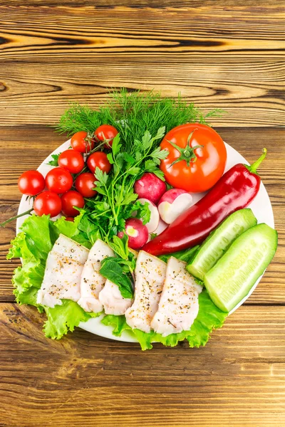 Plate with sliced fresh pork lard, fresh produce, vegetables on the wooden table.