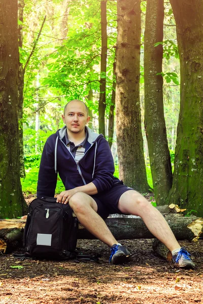 Hiker with backpack, young man stopped to rest in beautiful forest, summertime journey.