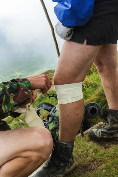 Men gives medical assistance to the tourist, wraps injured knee with white sports bandage.
