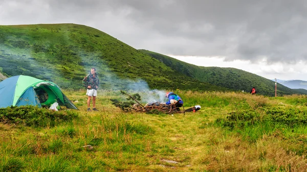 Camping tent and two men tourists at campfire in Carpathian mountains, summertime journey.