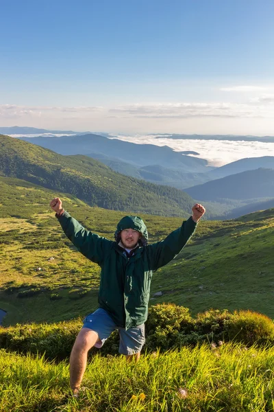 Young man standing on the top of mountain, holds hands up and shows victory emotion in sunrise time, Carpathians.