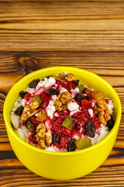 Sweet cottage cheese dessert with raspberry jam, nuts, raisins, candied in ceramic bowl on wooden table, space for text