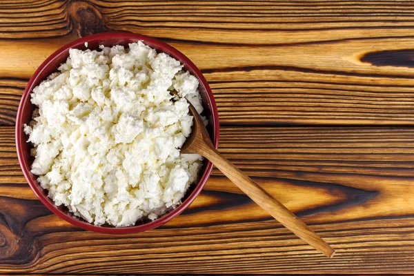 Fresh cottage cheese in ceramic bowl and spoon on wooden table, top view, with space for text