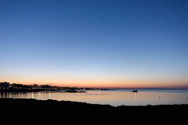Photo of beach and sea in protaras, cyprus island with hotels and a boat silhouettes, at sunset.