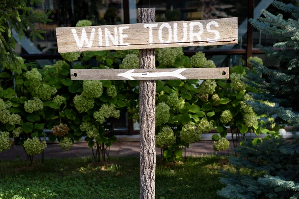 Wooden wine tour sign with arrow with green shrubs