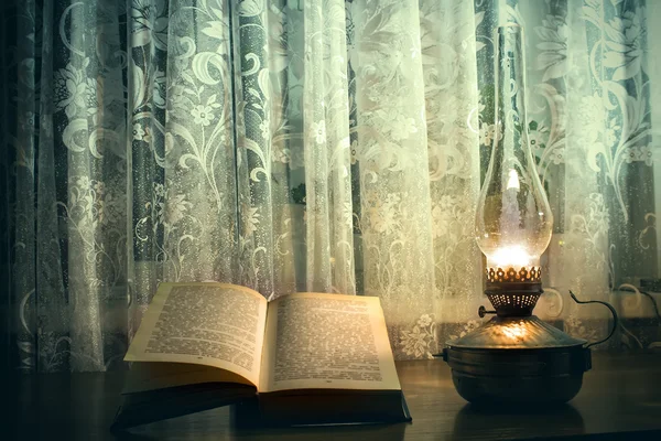 Old book on the table, a kerosene lamp and glass of wine