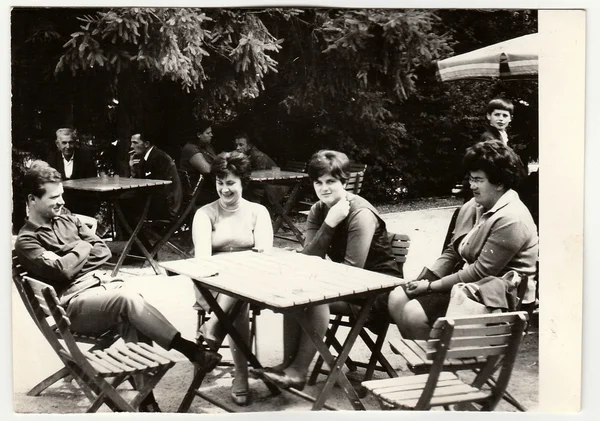 Vintage photo shows group of people sit at the garden restaurant.