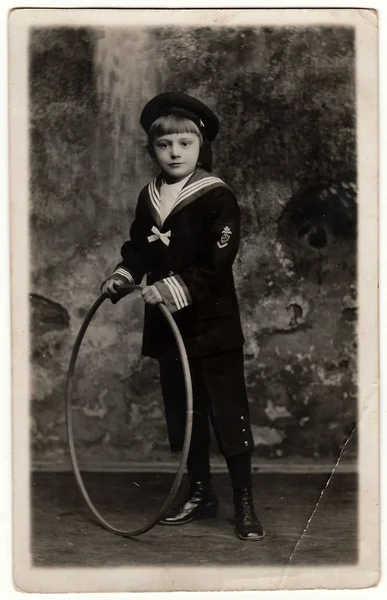 Vintage photo shows boy wears sailor costume with hoop. Antique black & white photo.