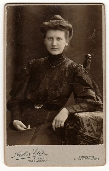 Vintage cabinet card shows woman with Victorian and Edwardian hair style sits at the table. Antique black & white photo.
