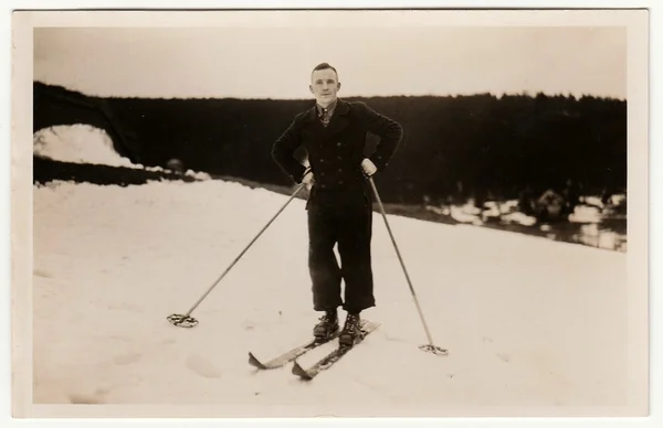 Vintage photo shows man stays on skis in the winter mountains.  Antique black & white studio portrait.