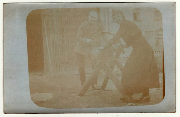 Vintage photo shows man and woman cutting a log. They work in the back yard. Photo has error obtained during photo process.  Antique black & white photo.