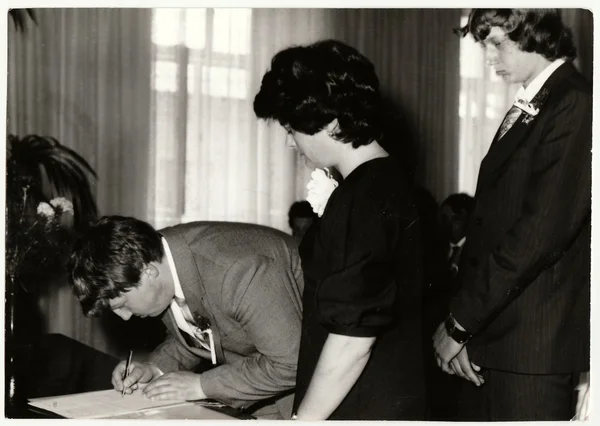 Vintage photo shows wedding's witness (best man) as he makes signature after wedding ceremnony. Black & white antique photo.