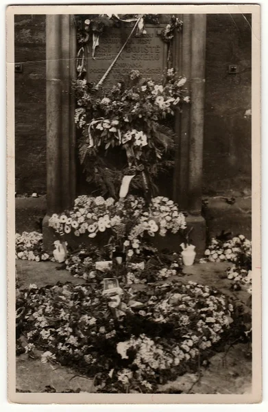 Vintage photo shows tomb with funeral wreath and flowers. Black & white antique photography.